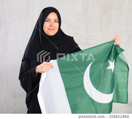 Balanced smiling Muslim woman in traditional black hijab holds flag of Pakistan 108822868