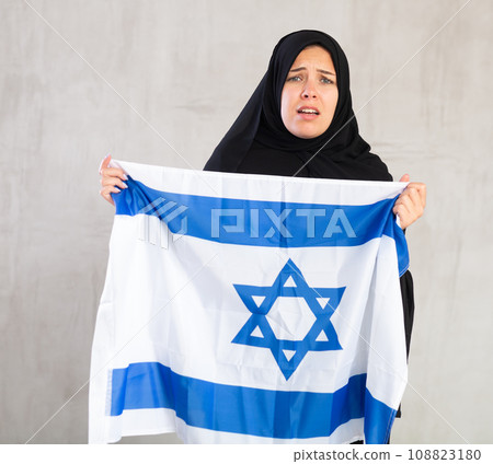 upset Muslim woman in traditional black hijab holds flag of Israel upset Muslim woman in traditional black hijab holds flag of Israel 108823180