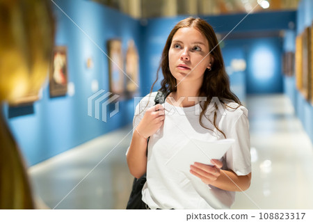 Girl visitor examines an exhibit standing in an art gallery 108823317
