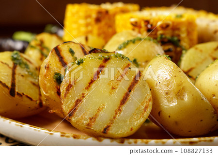 Baked potatoes, corn, lie on a large frying pan. Food court. Selective focus Baked potatoes, corn, lie on a large frying pan. Food court. Selective focus 108827133