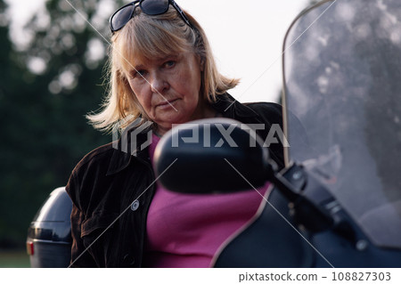 Hobby Motorcycle tourism. Looking at camera adult blonde motorcycle tourist, sitting on her bike. 108827303