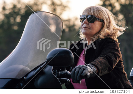 Confident pretty mature blonde in leather gloves driving her bike on autumn day. Hobby. Tourism. 108827304