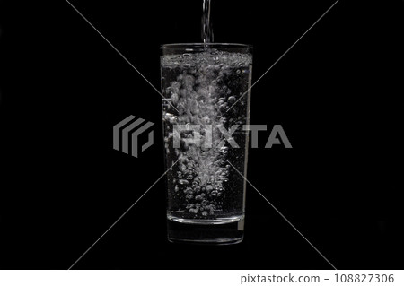 Image of water pouring into glass on black background. Image of water pouring into glass on black background. 108827306