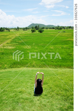 Asian woman in black shirt with jean sitting and stretch herself on grass field on mountain in lazy day and summer season. Asian woman in black shirt with jean sitting and stretch herself on grass field on mountain in lazy day and summer season. 108827626