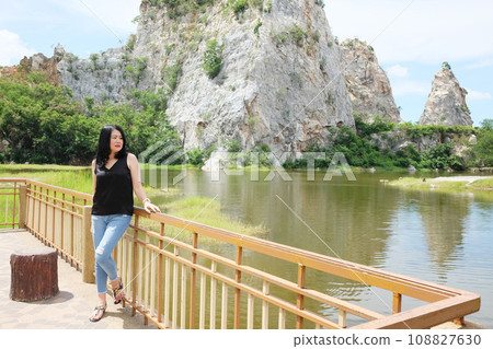Asian sexy woman and long hair in black shirt and jean smiling and standing on concrete bridge near rocky mountain, river and lake in natural sunlight and wind on summer season in the park. Asian sexy woman and long hair in black shirt and jean smiling and standing on concrete bridge near rocky mountain, river and lake in natural sunlight and wind on summer season in the park. 108827630