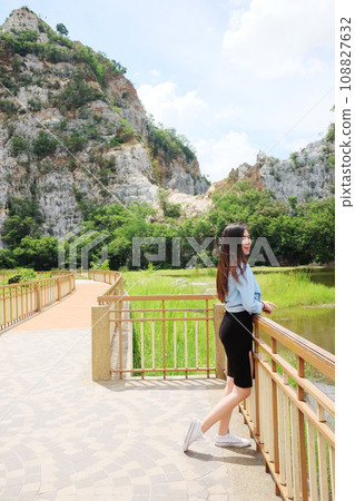 Asian sexy woman and long hair in black dress and jean jacket smiling and standing on concrete bridge near rocky mountain, river and lake in natural sunlight and wind on summer season in the park. 108827632