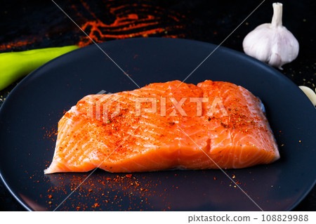 Raw salmon filet with rosemary and spices on plate, black stone background. Top view, flat lay 108829988