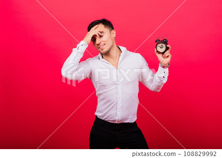 Emotional young man holding clock on red background. Being late concept 108829992