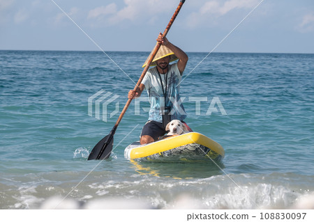 a guy on a sup board with a paddle with a dog stands on the sea in summer 108830097