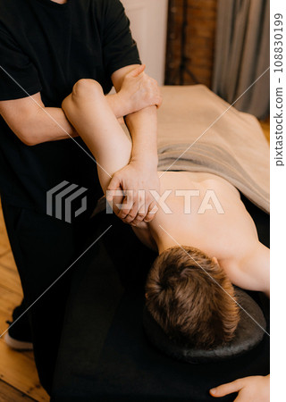 Physiotherapist massaging male patient with injured shoulder blade muscle. Sports injury treatment. 108830199