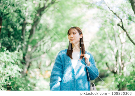 A woman walking along a tree-lined avenue of fresh greenery 108830303