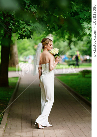 Beautiful and delicate bride in trousers and veil with a bouquet of white roses. Beautiful and delicate bride in trousers and veil with a bouquet of white roses. 108832086