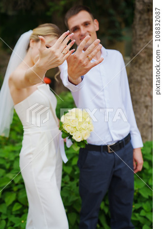 Gentle and happy newlyweds show wedding rings on hands on a walk in the park. Gentle and happy newlyweds show wedding rings on hands on a walk in the park. 108832087