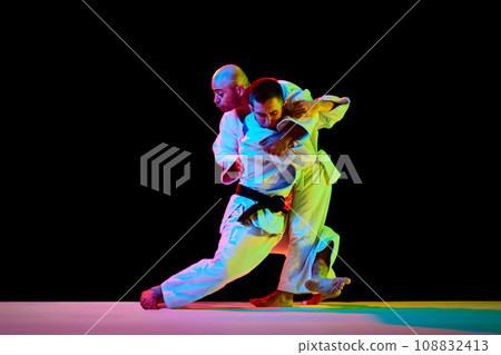 Two male professional sportsmen during match. Karate fighter attacking his opponent with leg technique isolated black background. 108832413