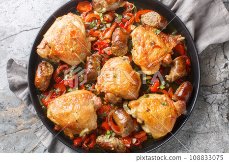 Braised chicken thighs, peppers and sausage in a vinegary, kind of spicy broth closeup on the plate. Horizontal top view Braised chicken thighs, peppers and sausage in a vinegary, kind of spicy broth closeup on the plate. Horizontal top view 108833075