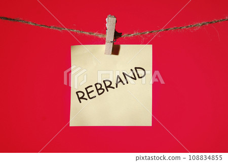 Rebrand text on a yellow sticker hanging on a rope with clothespins on a red background 108834855