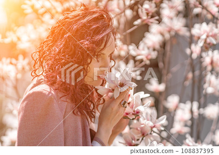 Magnolia park woman. Stylish woman stands near the magnolia bush in the park. Dressed in white corset pants and posing for the camera. 108837395