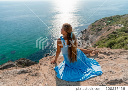 Woman travel sea. Happy woman in a beautiful location poses on a cliff high above the sea, with emerald waters and yachts in the background, while sharing her travel experiences 108837436