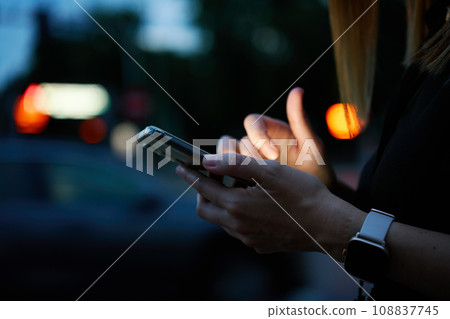 Close up shot of woman using smartphone on city street with bokeh lights at night. Mobile phone in female hands outdoors 108837745