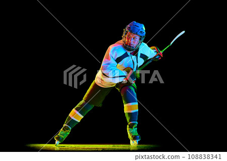 Competitive young girl, hockey player in motion during game, playing against black studio background in neon light 108838341