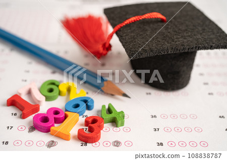 Graduation gap hat and pencil on answer sheet paper, Education study testing learning teach concept. Graduation gap hat and pencil on answer sheet paper, Education study testing learning teach concept. 108838787