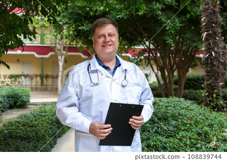 A thick-set blond male doctor with documents in the hospital yard A thick-set blond male doctor with documents in the hospital yard 108839744