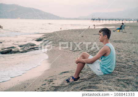 Boy teen sits on the beach and looks at the sea in Alanya city Boy teen sits on the beach and looks at the sea in Alanya city 108841333