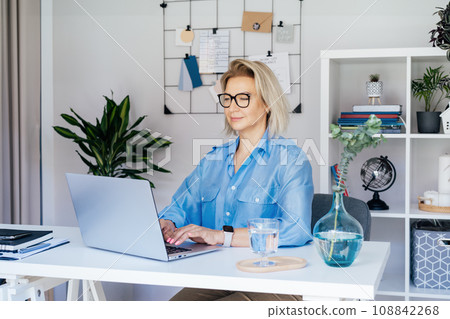Smiling mature businesswoman with laptop at her office workplace, confident middle-aged experienced senior female professional, CEO of company looking at camera. Female entrepreneur manage business Smiling mature businesswoman with laptop at her office workplace, confident middle-aged experienced senior female professional, CEO of company looking at camera. Female entrepreneur manage business 108842268