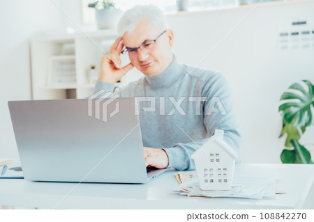 Focus on House model, money and docs on table and blurred senior man works on laptop. Housing cost and payments. Real estate, property investment. Home mortgage loan rate. Saving money for retirement Focus on House model, money and docs on table and blurred senior man works on laptop. Housing cost and payments. Real estate, property investment. Home mortgage loan rate. Saving money for retirement 108842270
