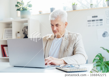 Concentrated grey hair middle-aged man working on laptop while sitting at his work place in office. Confident, experienced senior male professional. Corporate manager, entrepreneur manage business. Concentrated grey hair middle-aged man working on laptop while sitting at his work place in office. Confident, experienced senior male professional. Corporate manager, entrepreneur manage business. 108842271