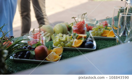 Fruit table for the holiday, Watermelon, orange and grapes. Buffet with fruits and drinks, champagne, juice. Catering with fresh fruit. Sweet natural food. Fruit table for the holiday, Watermelon, orange and grapes. Buffet with fruits and drinks, champagne, juice. Catering with fresh fruit. Sweet natural food. 108843590