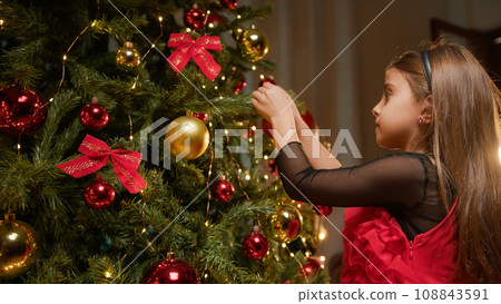 young baby girl putting a red ball to decorate Christmas tree young baby girl putting a red ball to decorate Christmas tree 108843591