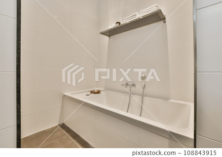 a modern bathroom with white tiles and black trim on the walls, there is a mirror in the wall above the bathtub 108843915