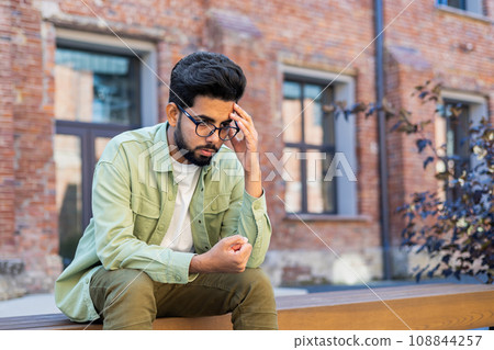 Sad depressed man sitting on bench outside office building, businessman disappointed with achievement results, unhappy man. 108844257