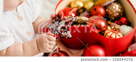 Banner Close-up Christmas Baby in Santa Hat, Child holding christmas bauble near Present Gift Box over Holiday Lights background Banner Close-up Christmas Baby in Santa Hat, Child holding christmas bauble near Present Gift Box over Holiday Lights background 108844258