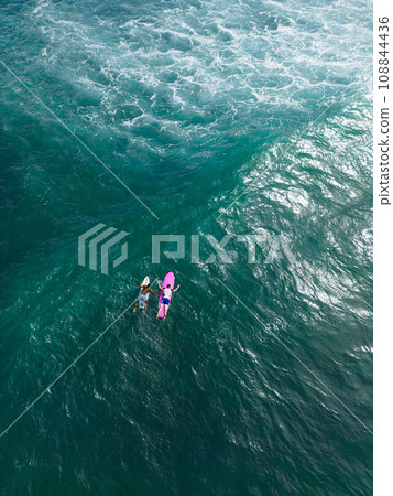 Aerial of two surfers paddling on boards over turquoise ocean waters, marine adventure and water sports from above. Athletes prepare to ride the waves. Freedom of the sea. 108844436