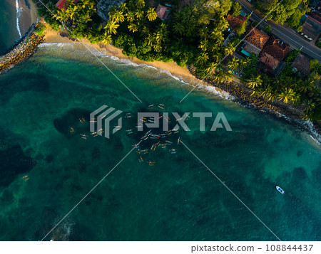 Top view of multiple oruwa outrigged canoe boats fishing in clear turquoise waters near a tropical shoreline, surrounded by lush greenery and a tranquil beach. Blue sea water. Fishermen catch fish. 108844437