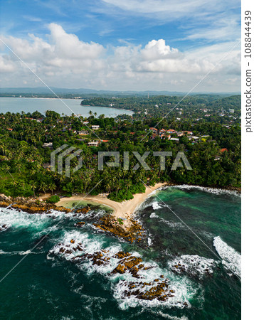 Tropical coastline with lush greenery meets the foamy waves of the turquoise sea, while a secluded sandy beach hints at a hidden paradise for would-be adventurers or romantic getaways. 108844439