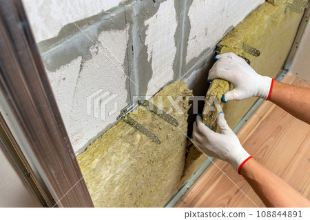 Worker insulating a room wall with mineral rock wool thermal insulation. 108844891