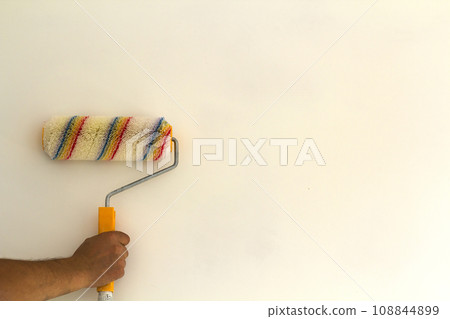 Worker hand with paint roller brush near wall in renovated room interior isolated on white background. Renovation and DIY concept. 108844899