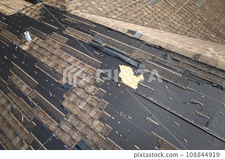 Wind damaged house roof with missing asphalt shingles after hurricane Ian in Florida. Repair of home rooftop concept 108844919