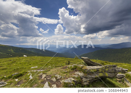 Wide panorama of lit by sun mountain plateau with green grass, patches of snow and big boulders on distant mountains under cloudy sky background. Beauty of nature, tourism and traveling concept. Wide panorama of lit by sun mountain plateau with green grass, patches of snow and big boulders on distant mountains under cloudy sky background. Beauty of nature, tourism and traveling concept. 108844943