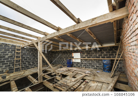 Two-storied building under construction and renovation. Perspective view of energy saving walls of large hollow foam insulation blocks and bricks, temporary wooden scaffolding, beams as roof frame. Two-storied building under construction and renovation. Perspective view of energy saving walls of large hollow foam insulation blocks and bricks, temporary wooden scaffolding, beams as roof frame. 108845106