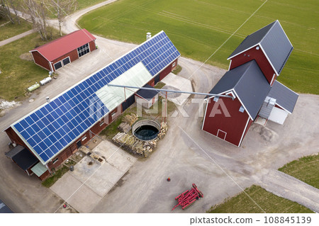 Top view of rural landscape on sunny spring day. Farm with solar photo voltaic panels system on wooden building, barn or house roof. Green field copy space background. Renewable energy production. Top view of rural landscape on sunny spring day. Farm with solar photo voltaic panels system on wooden building, barn or house roof. Green field copy space background. Renewable energy production. 108845139