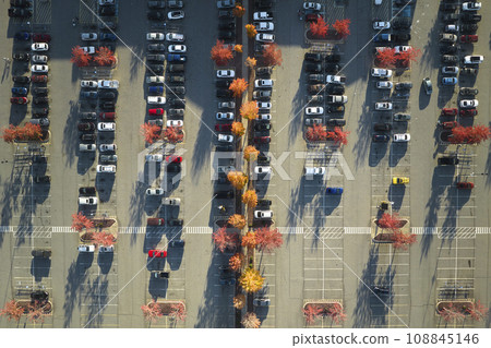 Top view of many cars parked on a parking lot in front of a strip mall plaza. Concept of consumerism and market economy 108845146