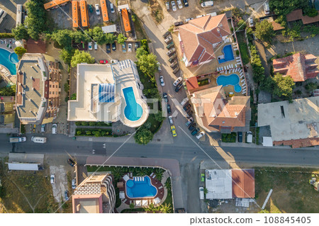 Top down aerial view of hotels roofs, streets with parked cars and swimming pools with blue water in resort city near the sea. Top down aerial view of hotels roofs, streets with parked cars and swimming pools with blue water in resort city near the sea. 108845405