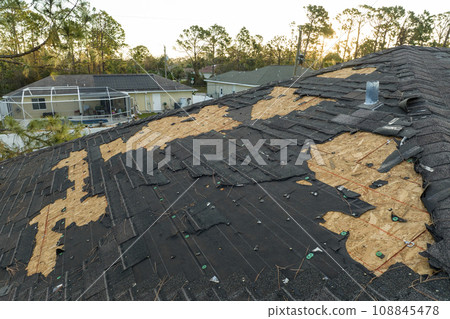 Ruined rooftop in need of repair. Wind damaged house roof with missing asphalt shingles after hurricane Ian in Florida Ruined rooftop in need of repair. Wind damaged house roof with missing asphalt shingles after hurricane Ian in Florida 108845478