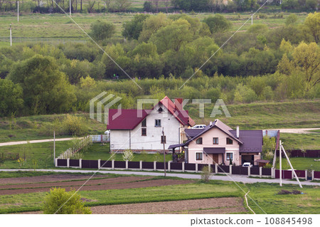 Quiet residential suburban area. Street with new modern comfortable brick cottages with yards and blooming gardens on background of beautiful green forest. Investments in real estate concept. Quiet residential suburban area. Street with new modern comfortable brick cottages with yards and blooming gardens on background of beautiful green forest. Investments in real estate concept. 108845498