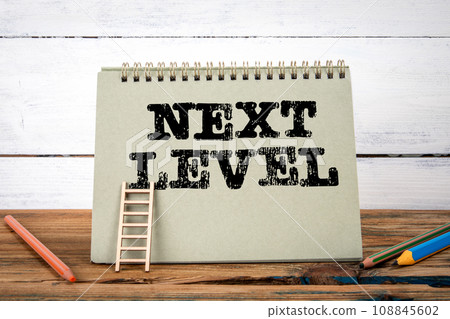 Next Level. Green notepad on wooden texture table and white background Next Level. Green notepad on wooden texture table and white background 108845602