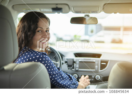 Portrait of attractive young woman in casual dress looking over her shoulder while sitting behind steering wheel driving a car 108845634